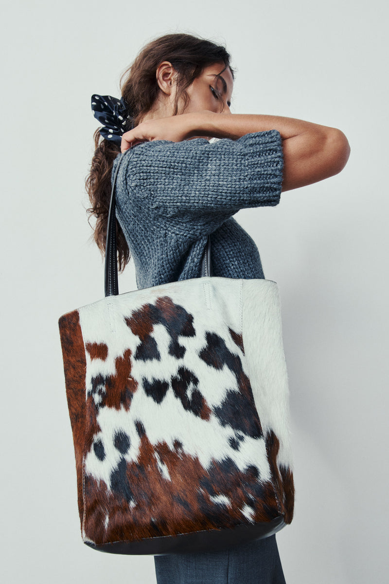 Person holding a tote bag with cow print design against a plain background