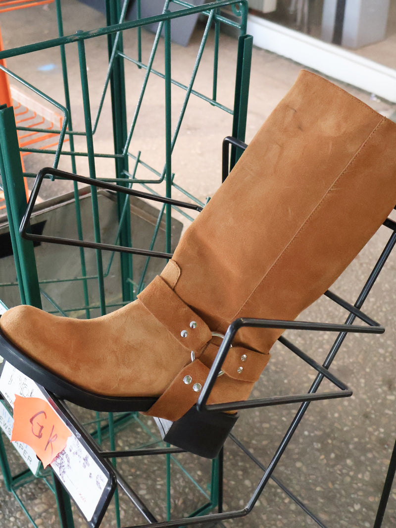 Tan boot displayed on a black metal stand with a price tag in the foreground.