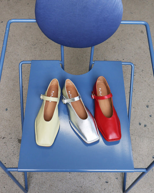 Three shoes (yellow, silver, red) on a blue chair outdoors.
